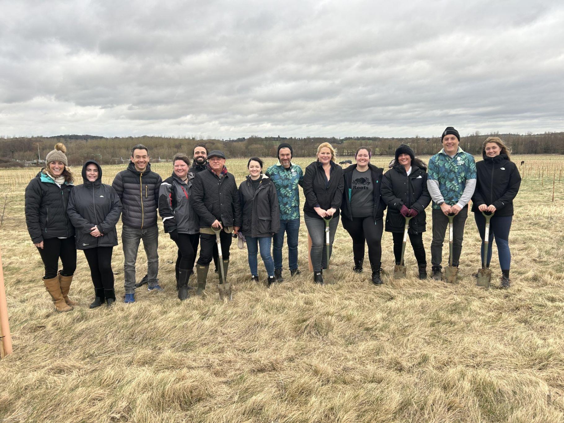 Fourteen members of the NCZ team standing together with spades on the planting site at the Forest of Marston Vale.